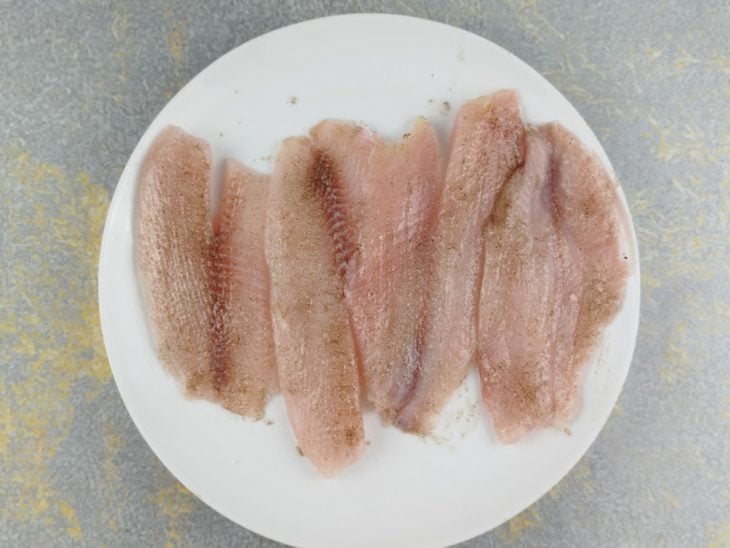 Filés de peixe sendo temperados com sal e pimenta-do-reino.