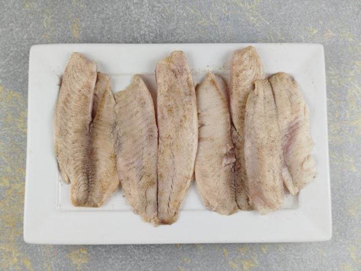 Peixes sendo selados em frigideira com azeite até dourarem levemente.