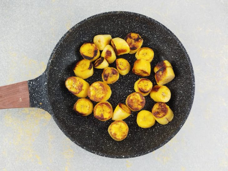 Bananas-da-terra sendo fritas na frigideira até ficarem douradas.