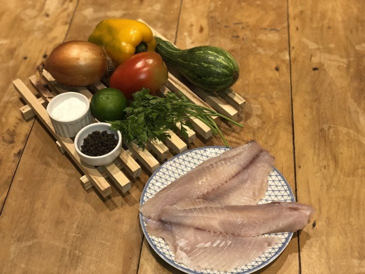 Ingredientes do peixe assado com legumes reunidos na mesa.