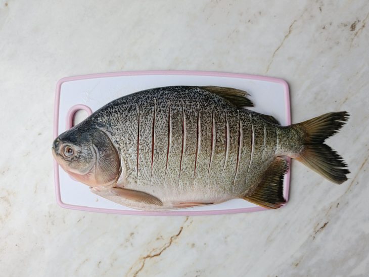 Peixe inteiro com cortes superficiais feitos dos dois lados.