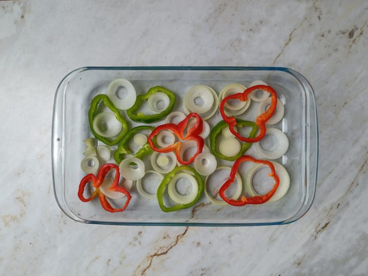 Assadeira com cebola e pimentões formando uma cama de vegetais.
