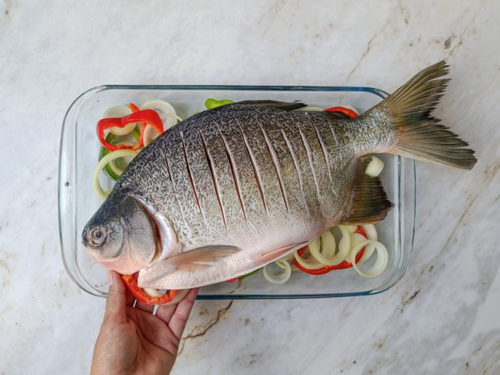 Peixe acomodado sobre os vegetais e recheado com cebola e pimentão.
