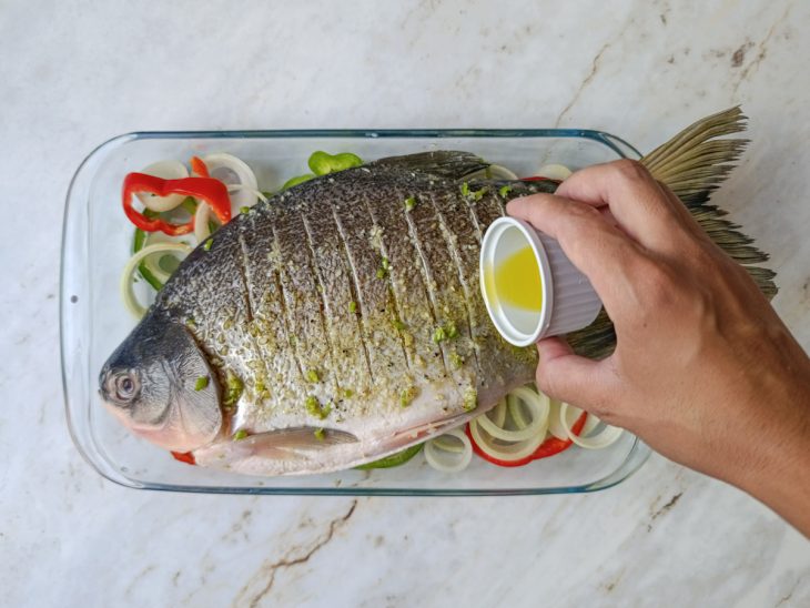Azeite sendo distribuído sobre o peixe antes de assar.