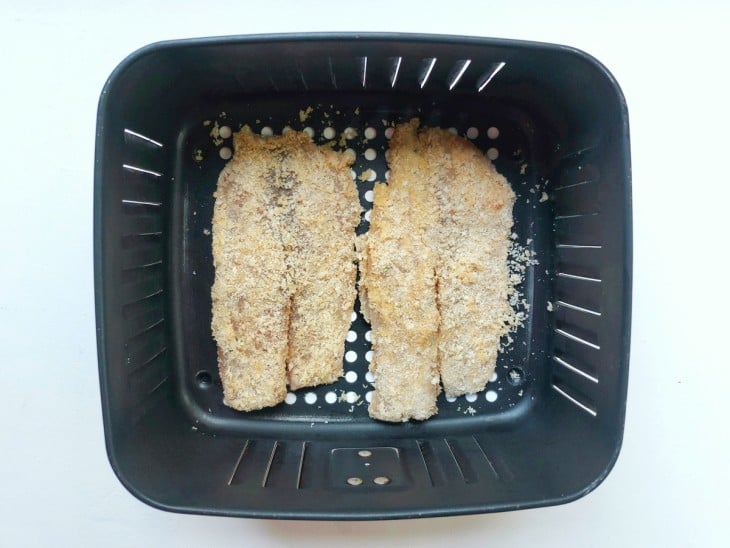 Os filés de peixe empanados dispostos no cesto da air fryer.