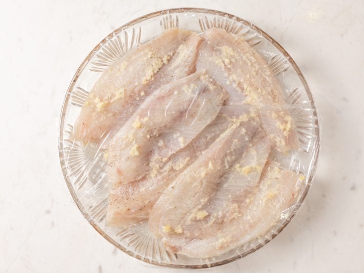 Peixe temperado em uma tigela coberta com plástico filme.