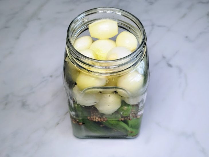 Um pote contendo sal, açúcar, coentro, minipepinos e minicebolas.