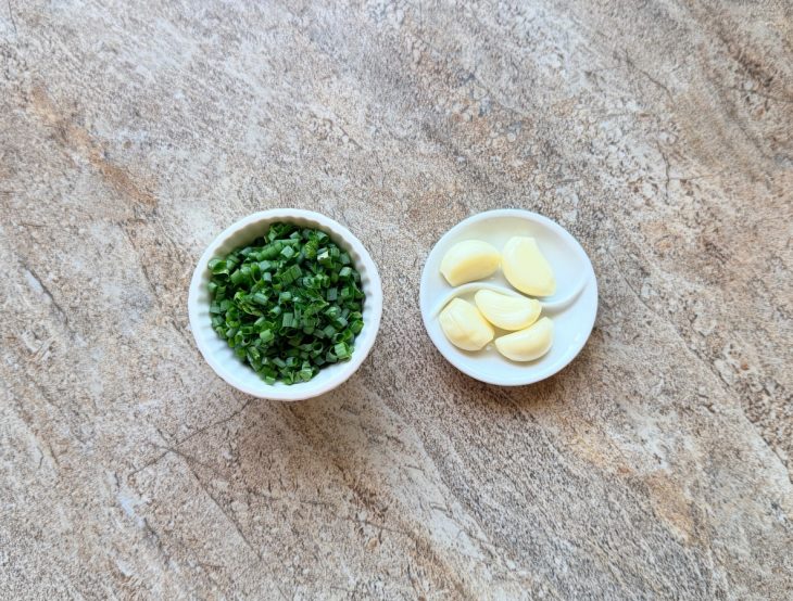 Dentes de alho descascados e cheiro-verde picado ao lado.
