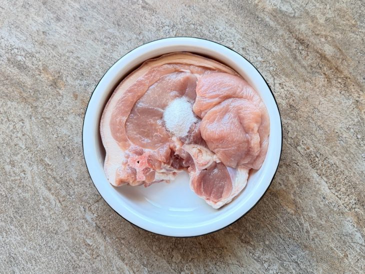 Pernil sendo temperado com sal em uma travessa.