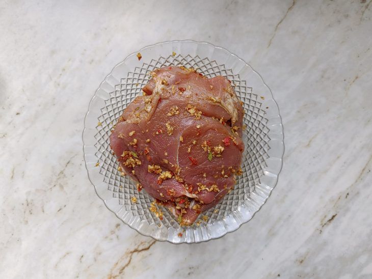 Pernil sendo completamente coberto pela pasta de temperos.