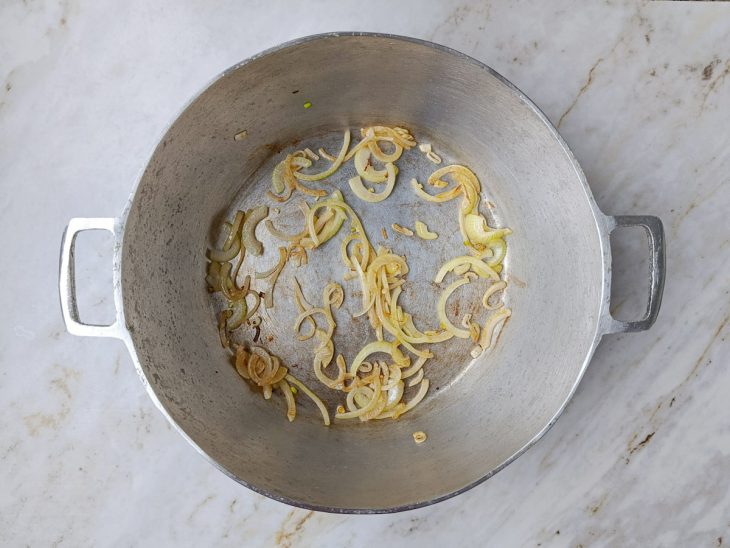 Cebola dourando na banha de porco em panela grande.