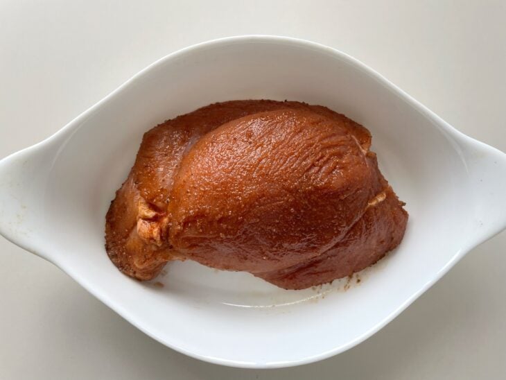 Carne suína crua recebendo massagem manual com a mistura homogênea de temperos por toda a sua extensão.
