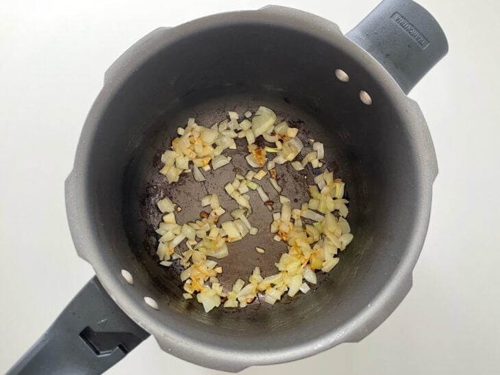 Cebola em cubos e alho amassado sendo refogados no fundo dourado deixado pela carne na panela.
