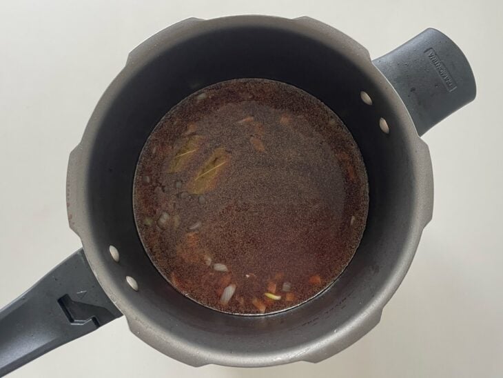 Líquidos e molho de tomate sendo despejados sobre o refogado aromático com a panela aberta.