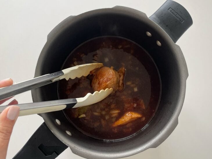 Pedaços de carne selados sendo devolvidos e acomodados no molho espesso dentro da panela.