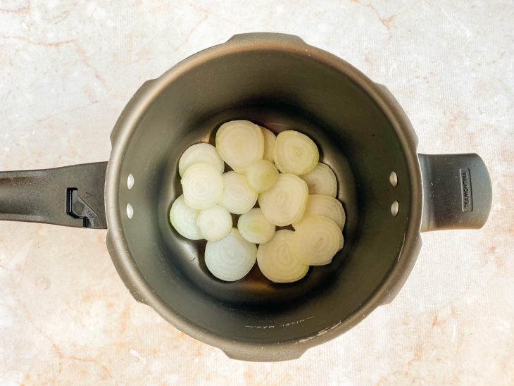 Cebolas em rodelas dentro da panela de pressão.