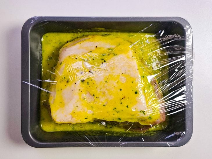 Assadeira com pernil temperado coberta com plástico-filme.