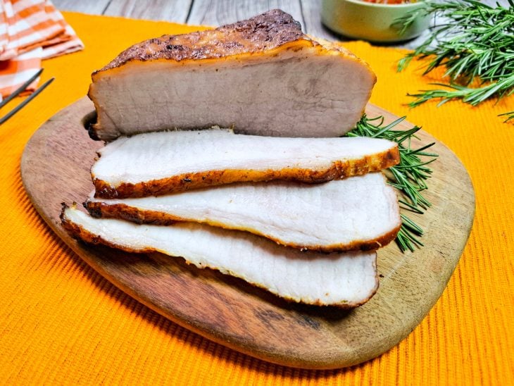 Pernil suíno na air fryer pronto para consumo e algumas fatias já cortadas sobre uma tábua de cozinha.