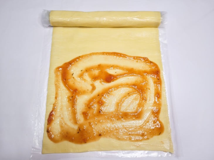 Uma massa de pastel aberta com molho de tomate espalhado.