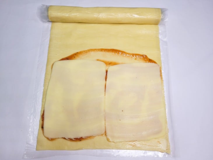 Uma massa de pastel aberta com molho de tomate espalhado e uma camada de mussarelas.