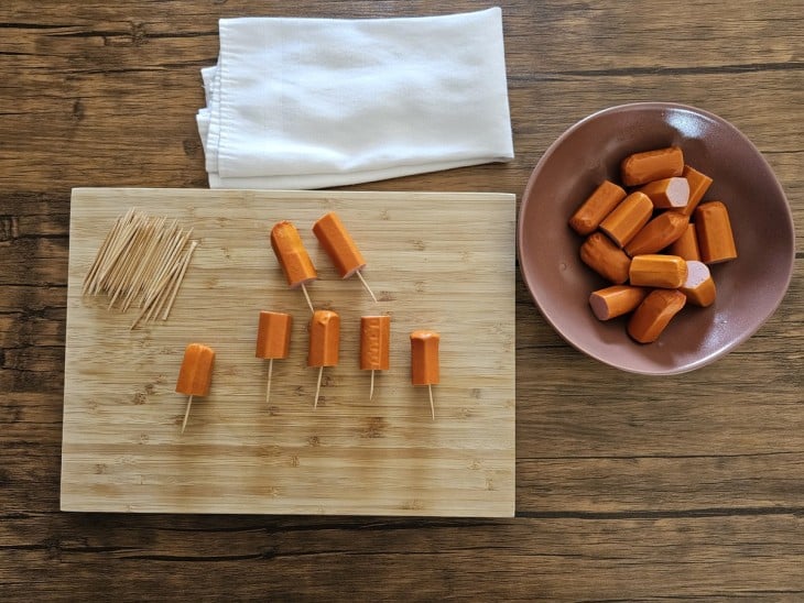 Uma tábua com salsichas cortadas ao meio e espetadas com palitos.