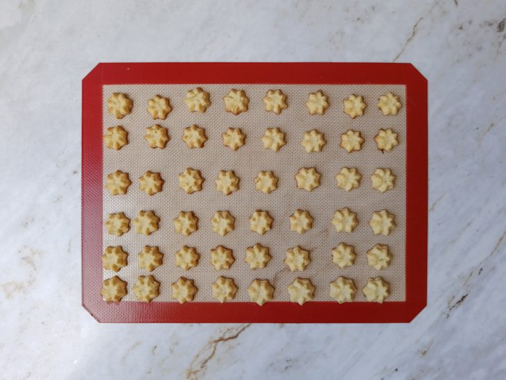 Petit fours modelados com saco de confeitar sobre a assadeira.