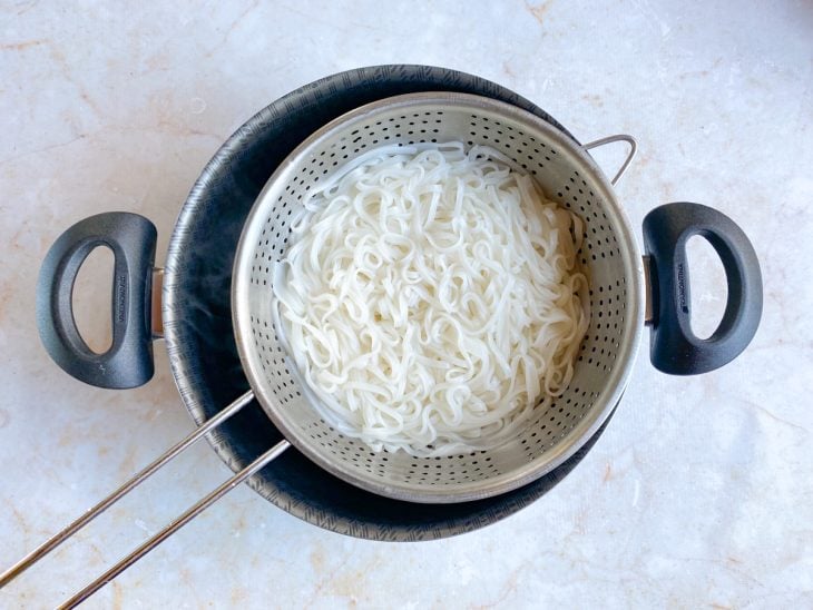 Uma peneira com o macarrão cozido sendo escorrido.