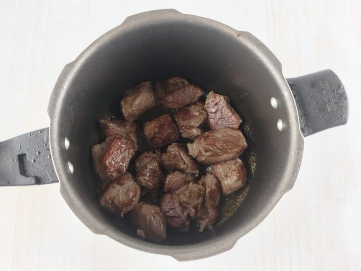 Carne em cubos sendo selada na panela de pressão com óleo.