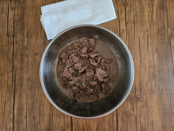 Tigela com cubos de carne cozidos e caldo com coloração escura junto.