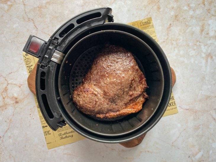 Uma cesta de airfryer contendo uma peça de picanha temperada.