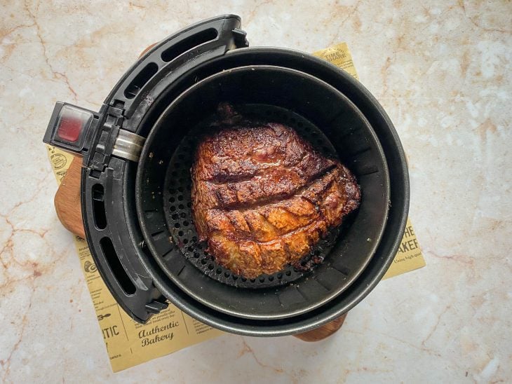 Uma cesta de airfryer contendo uma peça de picanha temperada.