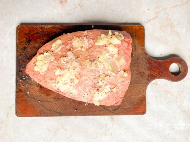 Na tábua, do lado da gordura, picanha com manteiga, pimenta-do-reino e sal grosso.