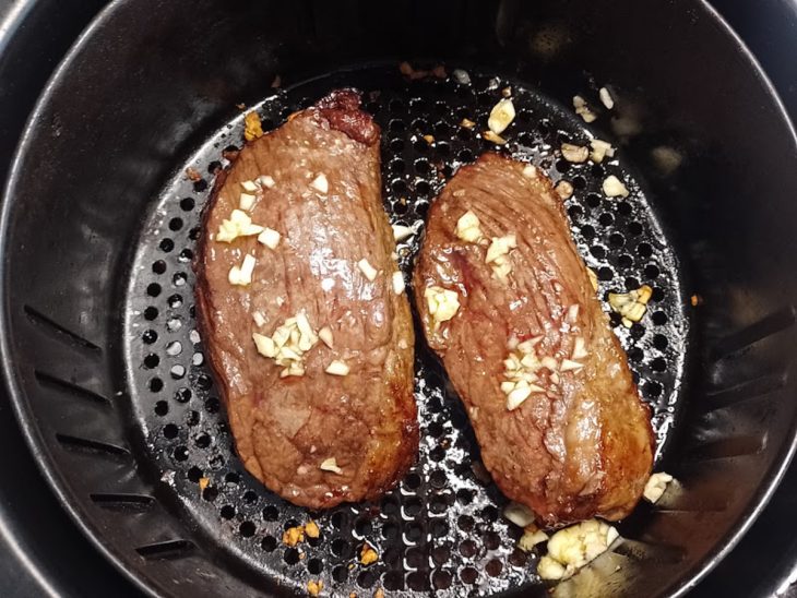 Bifes de picanha com manteiga de alho em um cesto de airfryer.