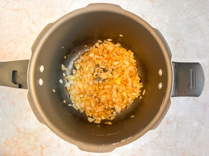 Manteiga, cebola e alho refogados na panela.