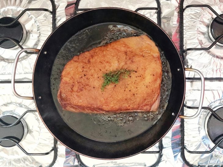 Uma peça de picanha com tomilho selando na panela.