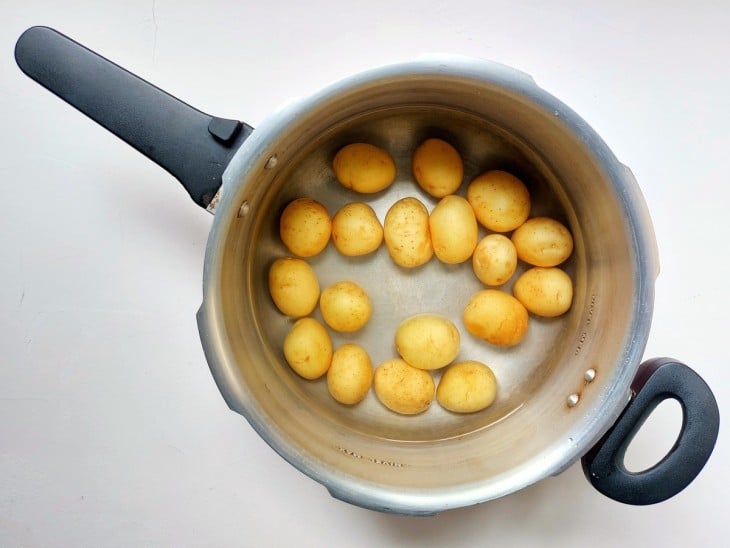 Uma panela de pressão contendo água e batatas-bolinhas.