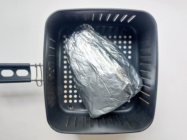 Uma cesta de airfryer contendo a peça de picanha embrulhada no papel alumínio.