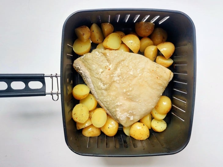 Uma cesta de airfryer contendo picanha suína com batatas.
