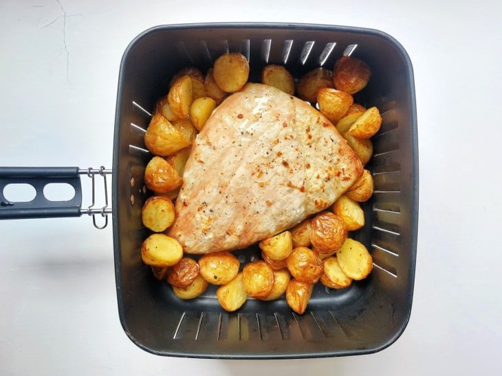 Uma cesta de airfryer contendo picanha suína com batatas.