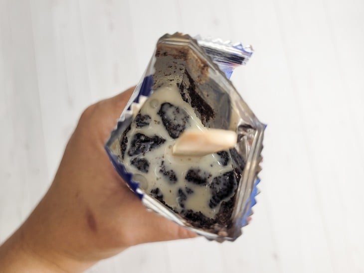 Um pacotinho de bolacha Oreo aberto com o creme dentro e um palitinho de sorvete.