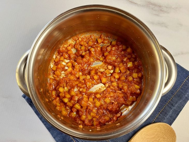 Uma panela refogando cebola, alho, pimentão, tomate e pimentas.