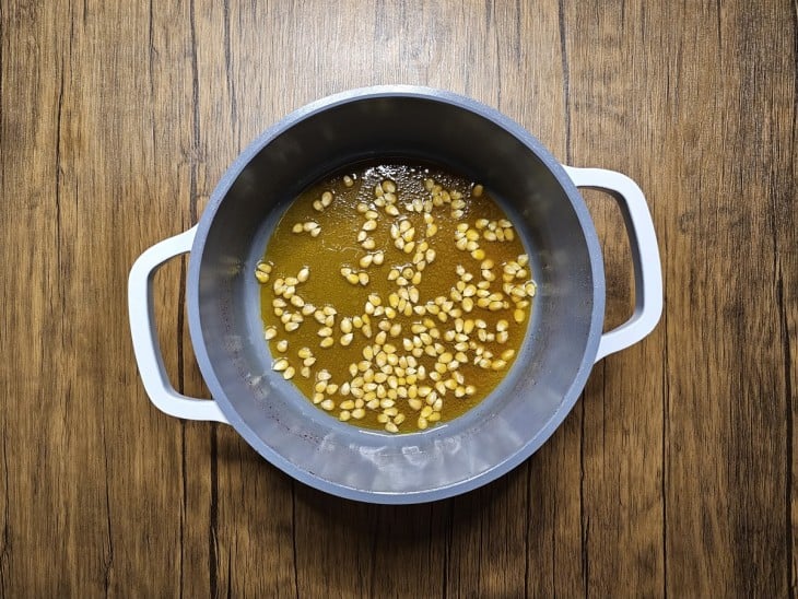 Parte da pipoca com corante amarelo dentro de uma panela cinza com as alças brancas