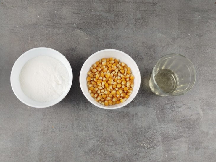 Ingredientes organizados na bancada com milho de pipoca, óleo e açúcar separados.