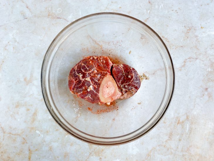 Temperos adicionados sobre a carne numa tigela de vidro redonda.