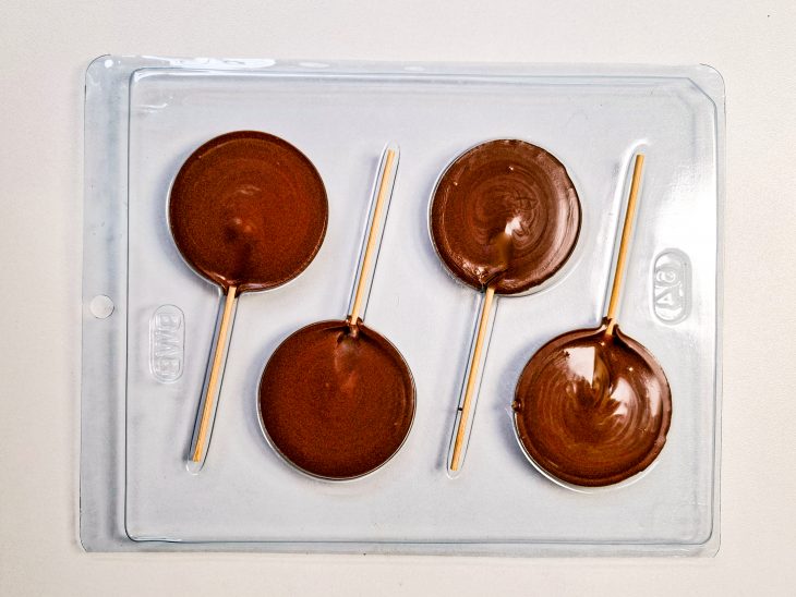 Nos moldes, os palitos colocados para formar o cabo do pirulito.