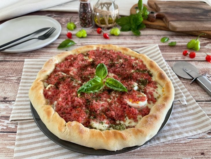 Pizza pronta e servida, decorada com folhas de manjericão.