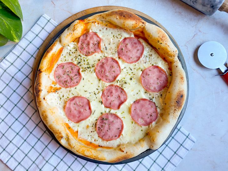 Pizza saída do forno, com bordas douradas e queijo derretido.