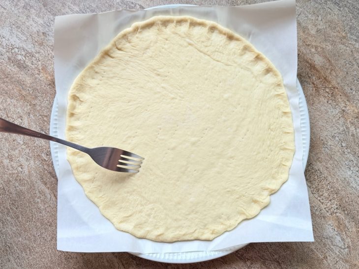 Massa aberta na forma, garfo fazendo furos.