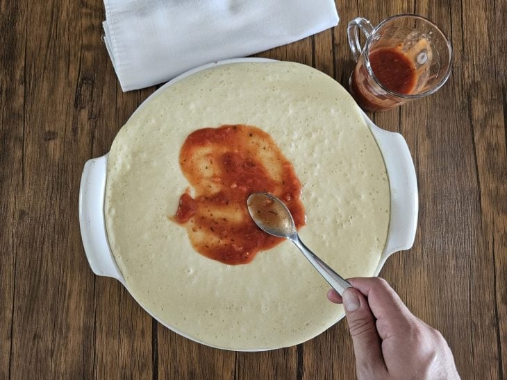 Molho de tomate sendo espalhado por cima da massa de pizza.