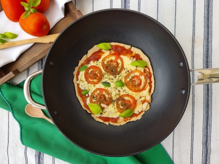 Pizza de queijo e tomates em uma frigideira preta.